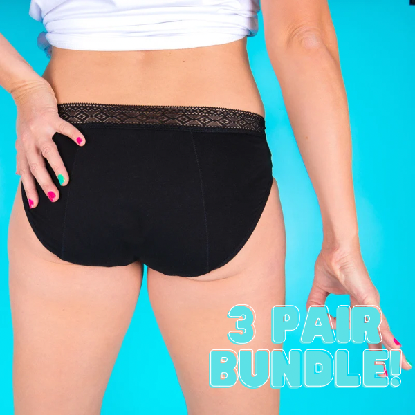 The model wears black low rise period pants with a lace waistband and a white T shirt, knotted and showing her lower back. She has her hands on her hips. The background is bright turquoise